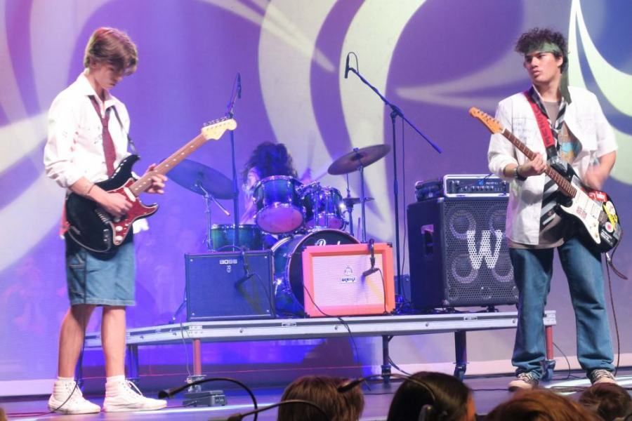 Two young men are playing guitars on stage in front of a crowd