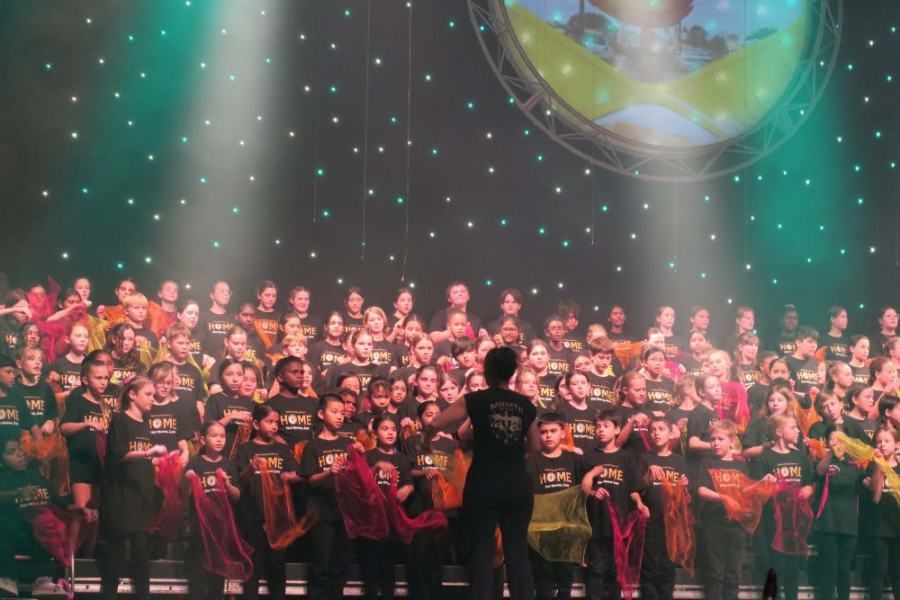 A man is standing in front of a large choir on a stage.