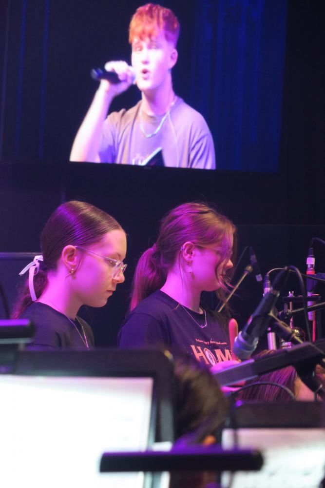 A man is singing into a microphone in front of two women