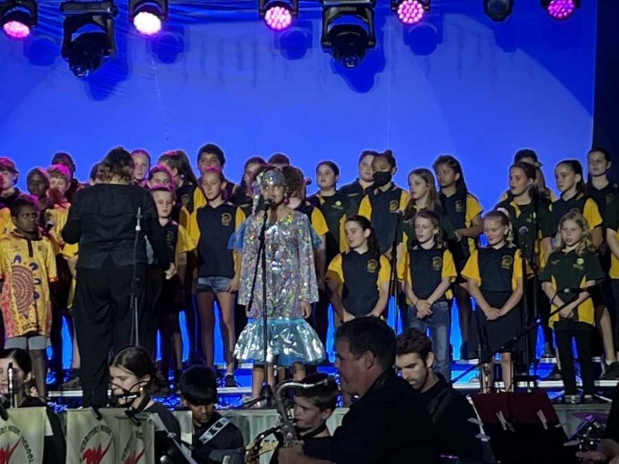 A choir is performing on a stage with a woman singing into a microphone
