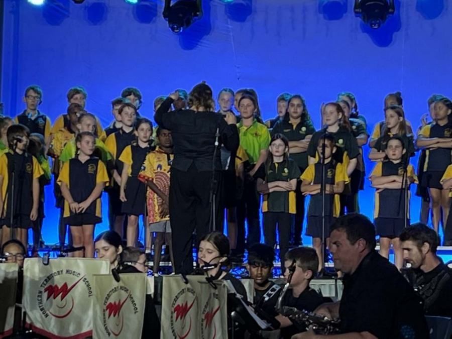 A choir is performing on stage with a man playing a guitar in the foreground