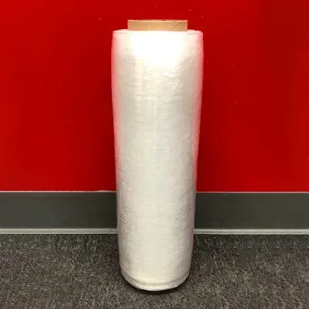 A roll of clear plastic wrap on a cardboard core, against a red wall.