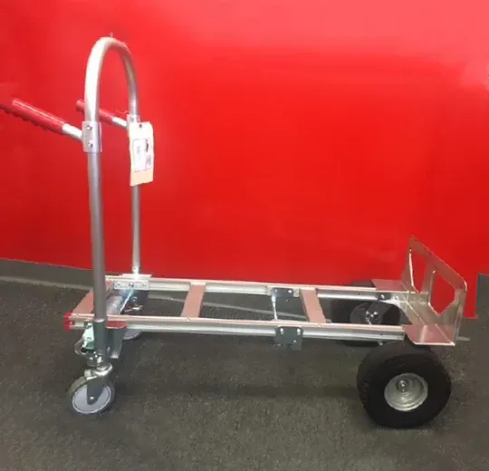 A silver hand truck with two large wheels and two smaller caster wheels against a red wall.
