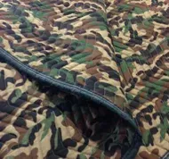 Camouflage-patterned blanket with dark border, quilted stitching.