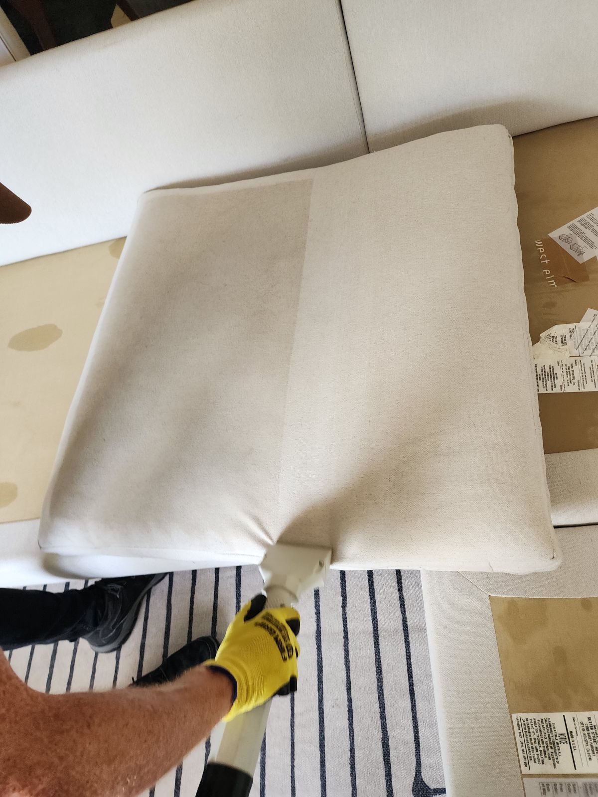 Person lifting a white upholstered cushion from a cardboard box on the floor