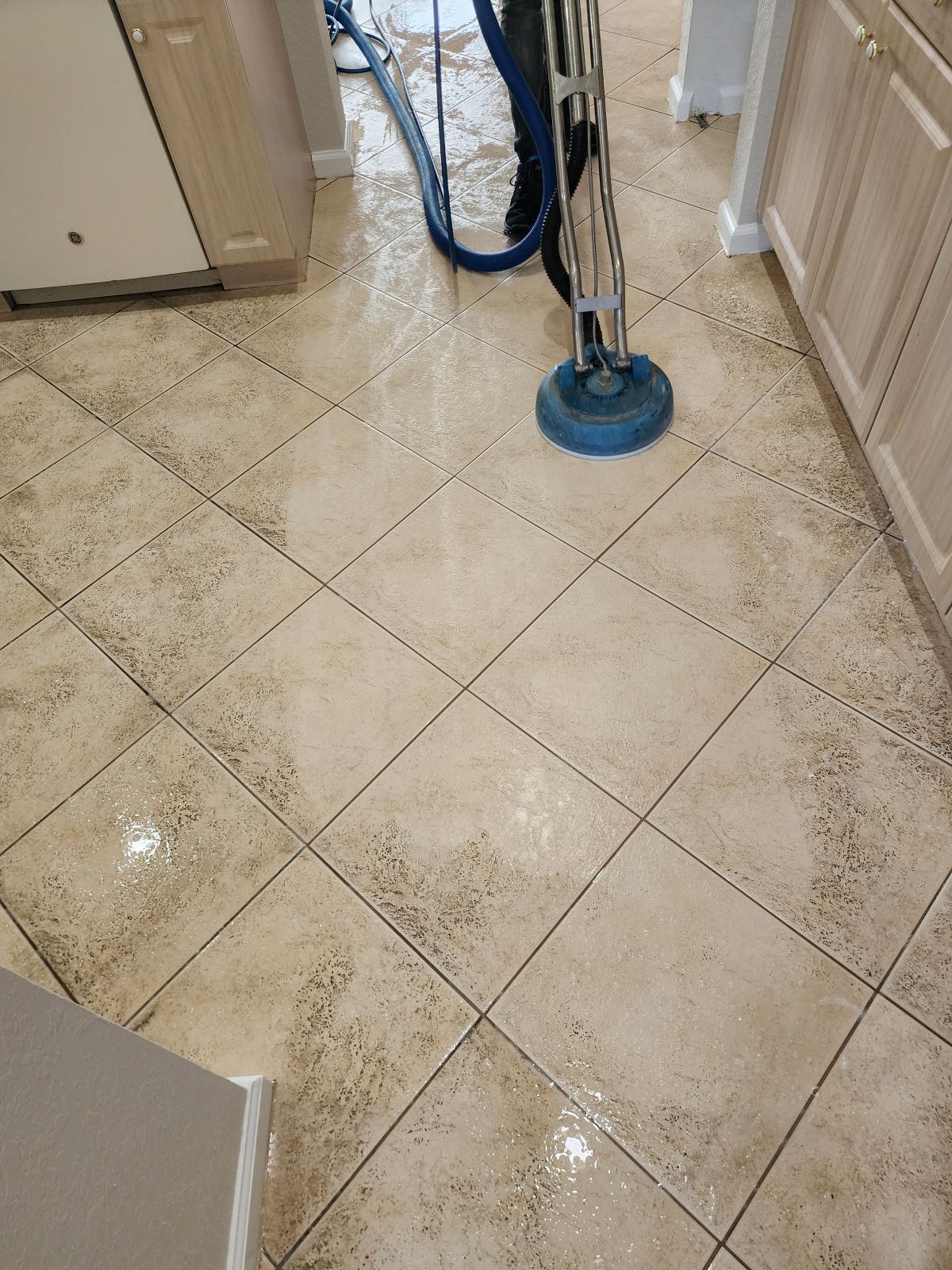 Blue floor-cleaning machine on a beige tiled floor in a hallway, with cleaning solution visible.