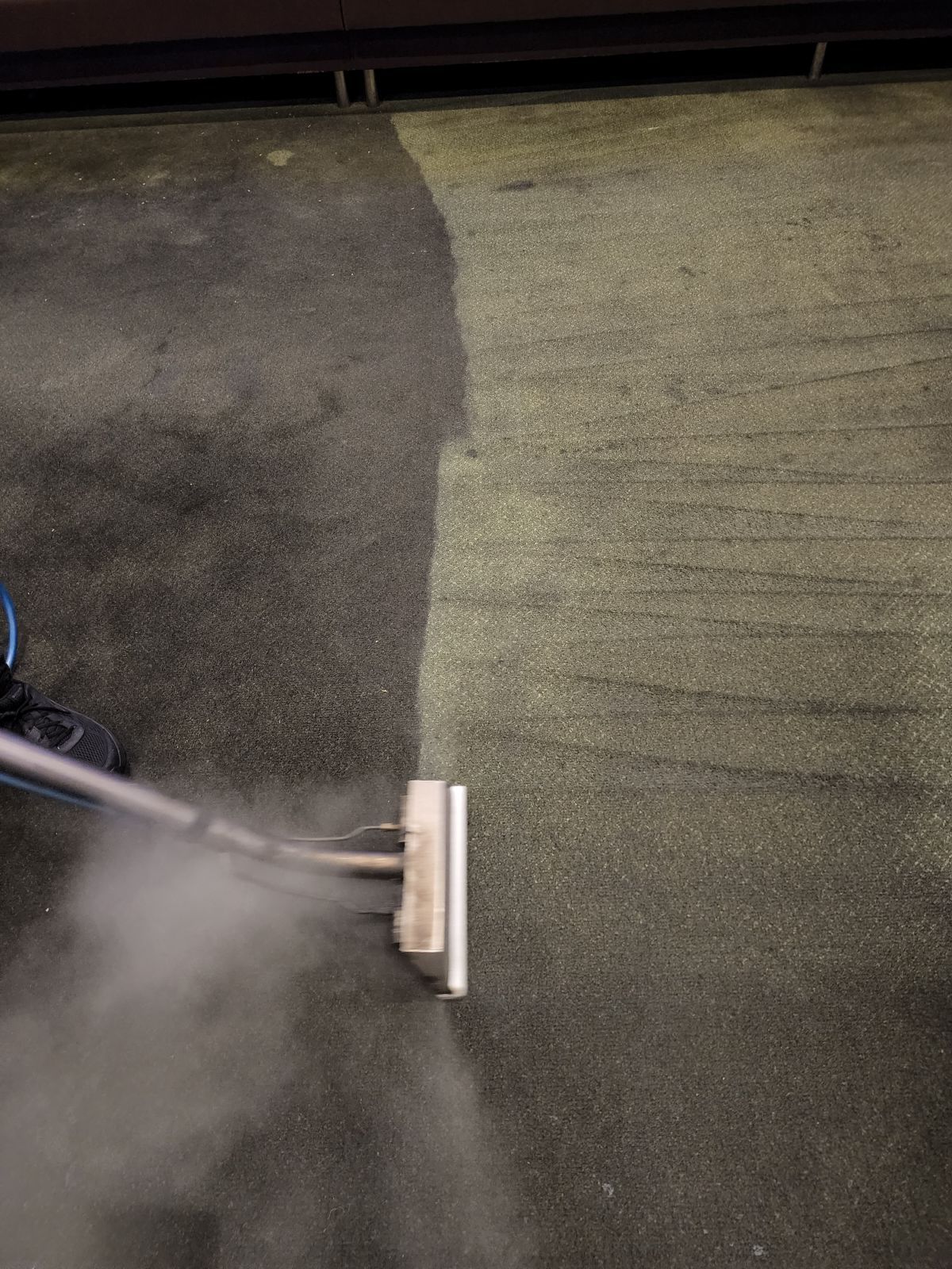 Carpet cleaner spraying steam on a green and gray carpet, creating a wet cleaned strip.