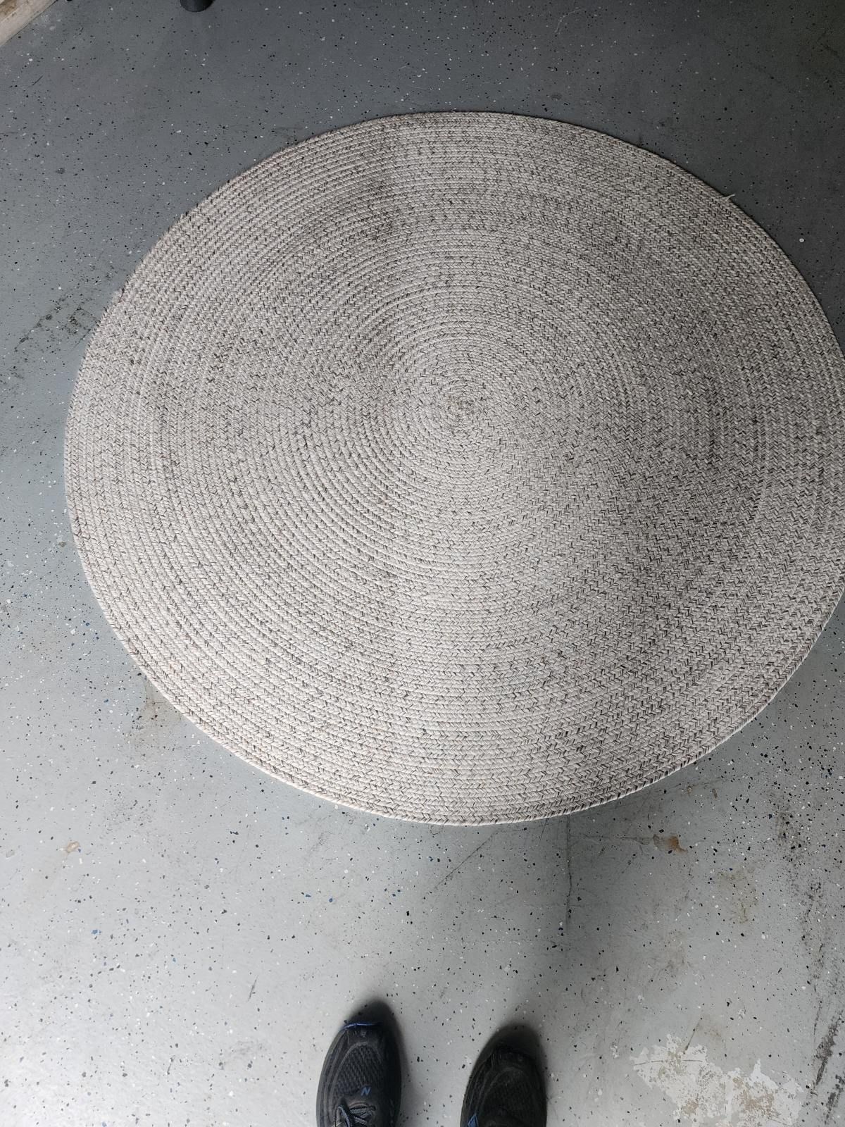 Round light-gray rug on a speckled floor, with the tip of a black shoe visible at the bottom.