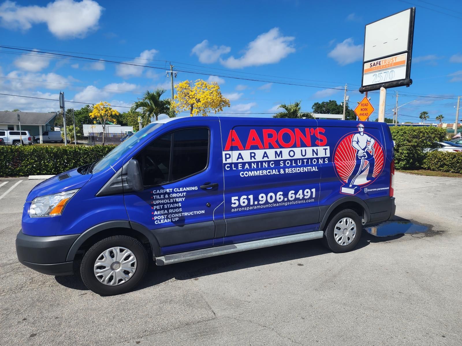 Blue Aaron's Rentals van parked in a lot under a bright sky, with company branding on the side.