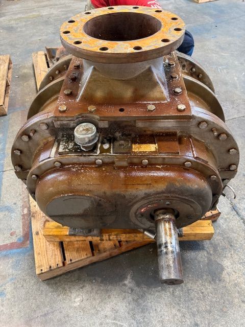 Rusty industrial pump on a wooden pallet, with flanged openings and a protruding metal shaft.