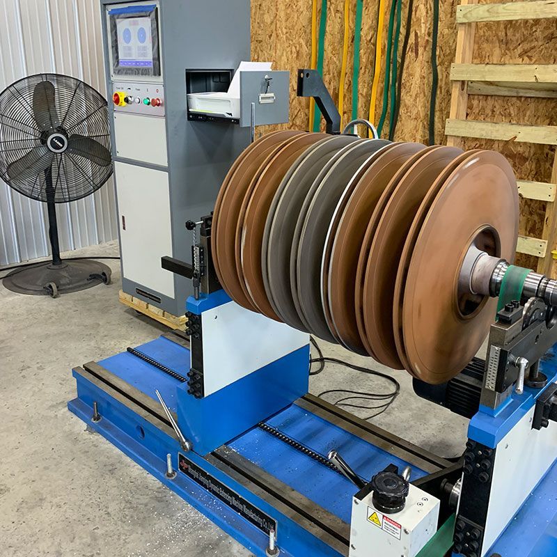 Industrial machine with stacked brown belts on a blue base in a workshop, beside a control panel and fan