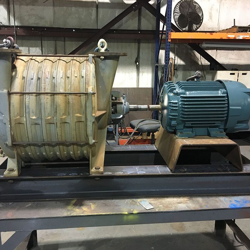 Industrial motor and pump assembly on a factory floor, with a blue electric motor connected to a large metal drum.