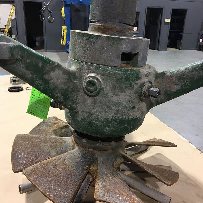 Close-up of a rusty green industrial metal impeller or mixer blade assembly in a workshop.