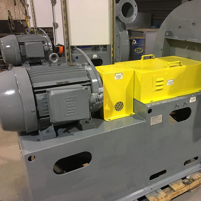 Industrial electric motor with bright yellow safety cover mounted on a gray machine base in a workshop.