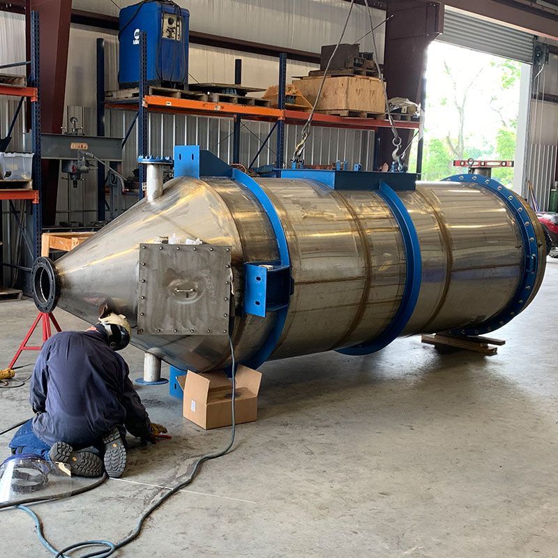 Worker welding a large cylindrical metal tank in a workshop