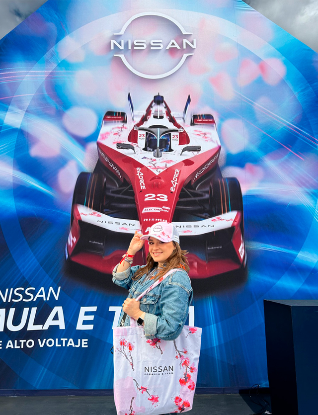 Mujer con chaqueta vaquera y sombrero de vaquero posando frente a una exhibición de un coche de carreras Nissan de Fórmula E.