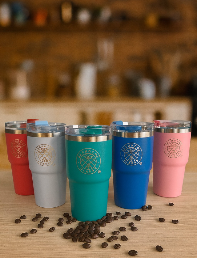 Cinco coloridos vasos de café reutilizables con tapa sobre una mesa de madera, con granos de café esparcidos alrededor.