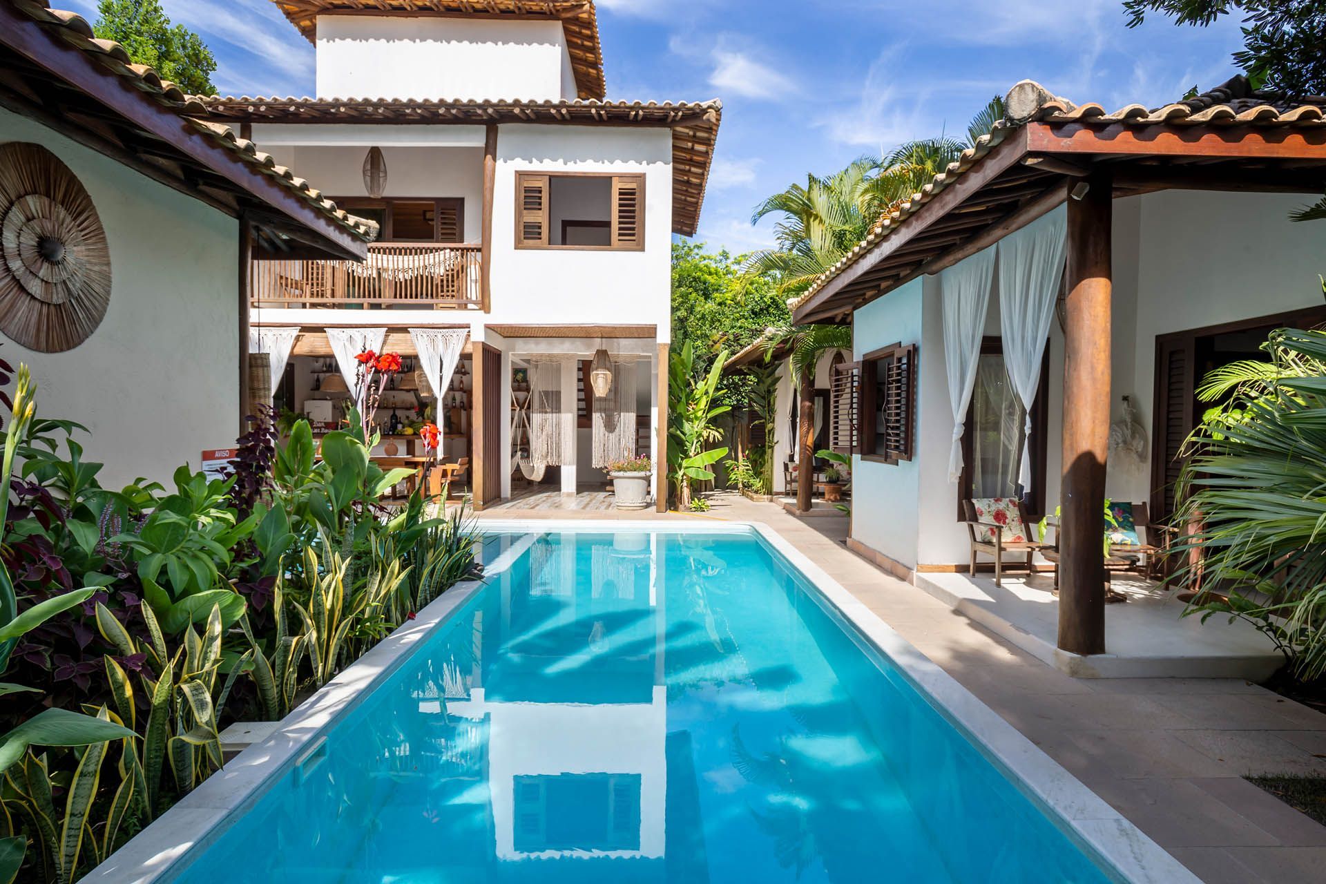 Pátio de uma villa moderna com piscina turquesa, plantas tropicais e céu azul.