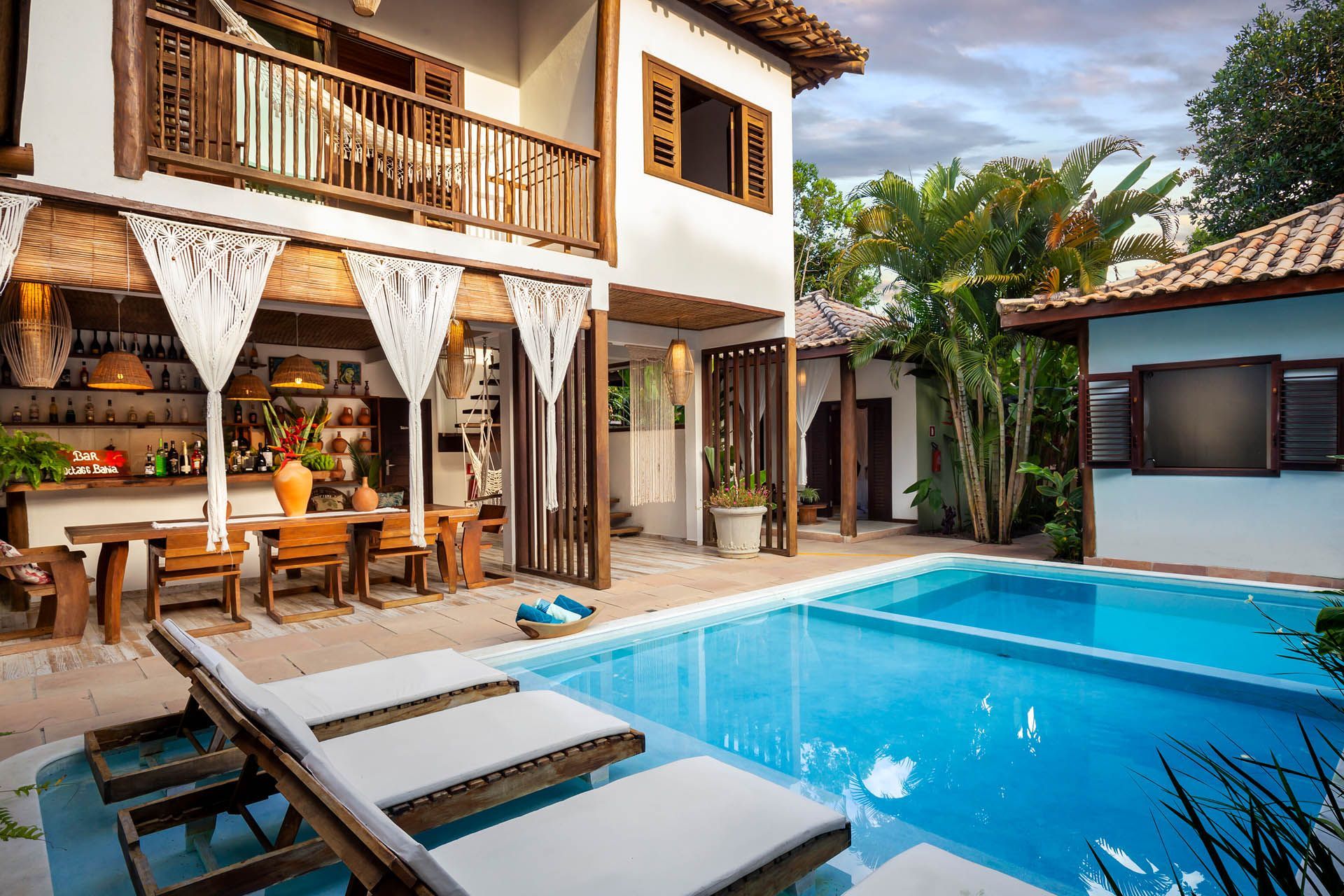 Pátio de villa de luxo com piscina azul, espreguiçadeiras e área de jantar externa coberta.