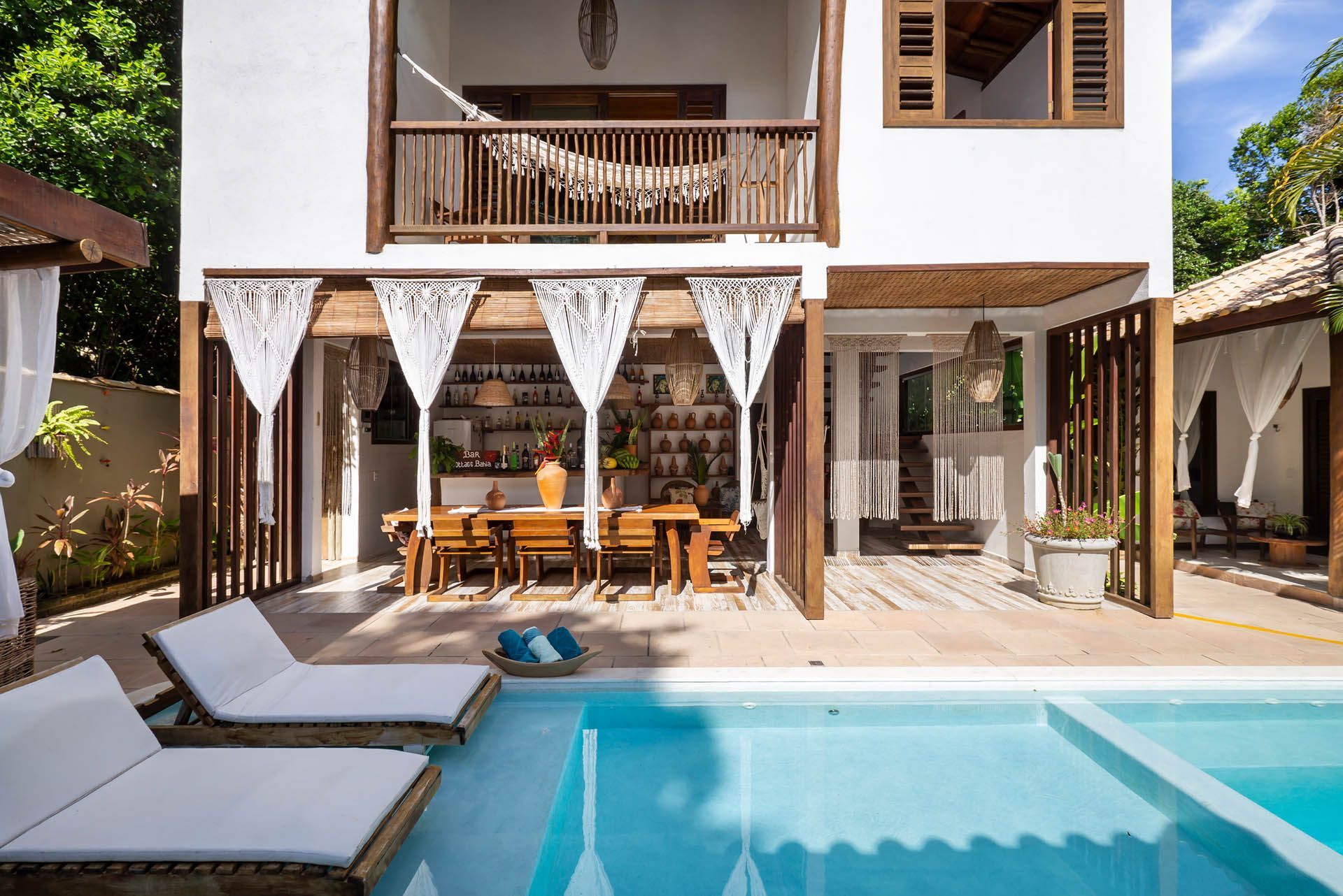 Moradia moderna com piscina turquesa, espreguiçadeiras e um pátio sombreado com mesa de jantar e varanda.