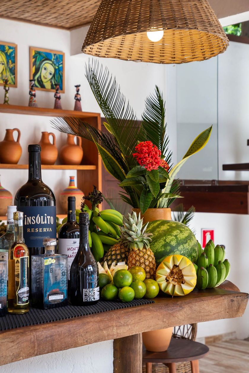 Exposição de frutas tropicais e garrafas de bebidas alcoólicas em uma prateleira de madeira em um restaurante bem iluminado.