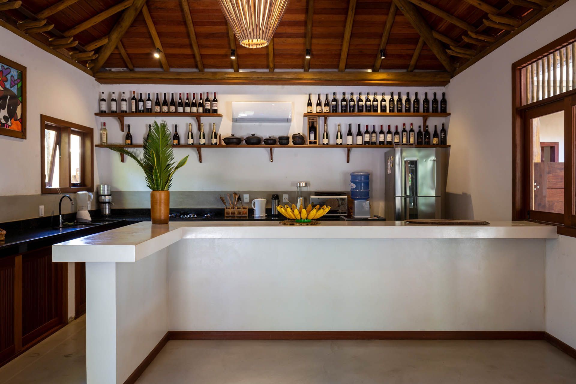 Interior de bar moderno com balcão branco, prateleiras de garrafas e teto de madeira.