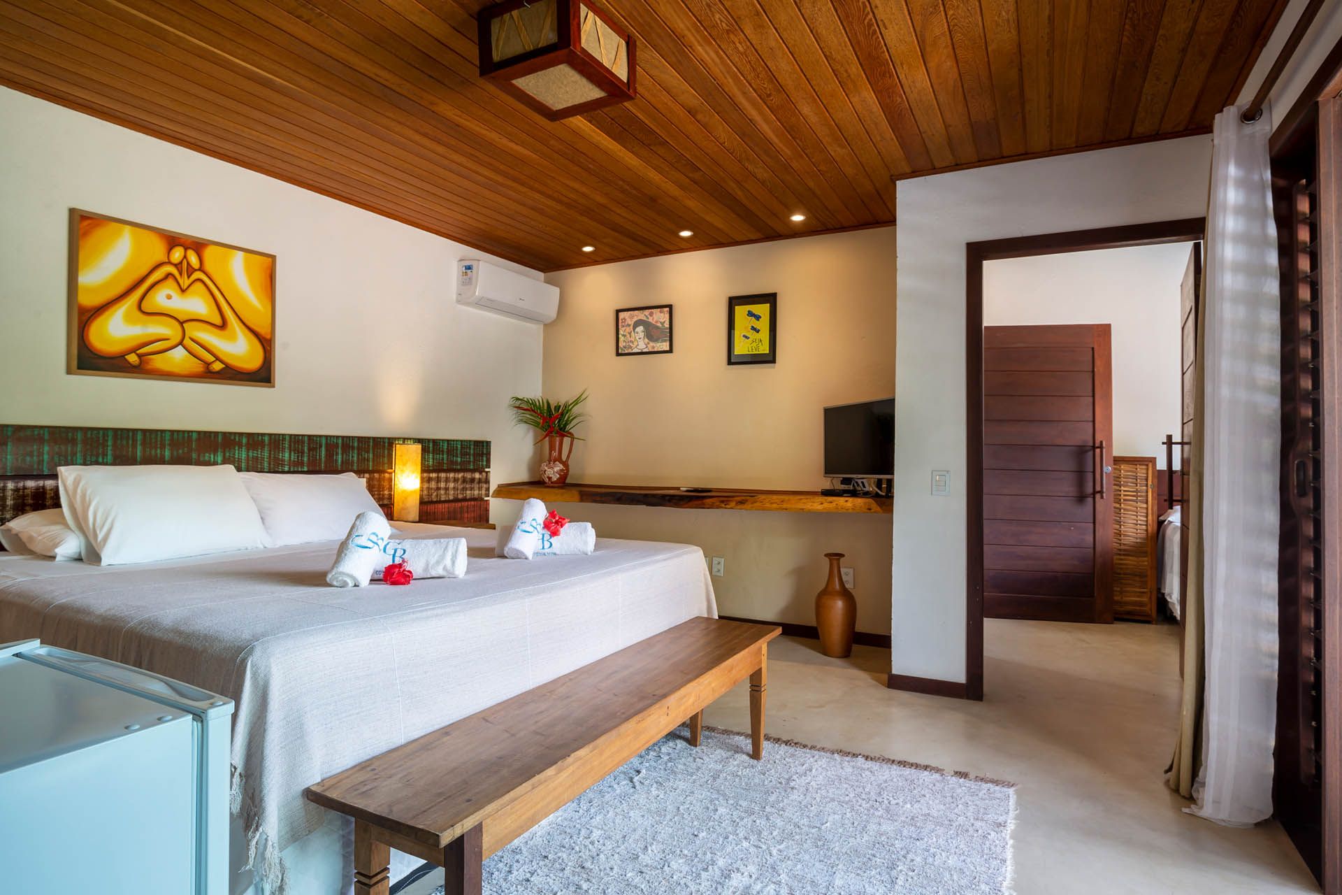 Quarto moderno e luminoso com uma cama grande, teto de madeira e vista para um quarto adjacente.
