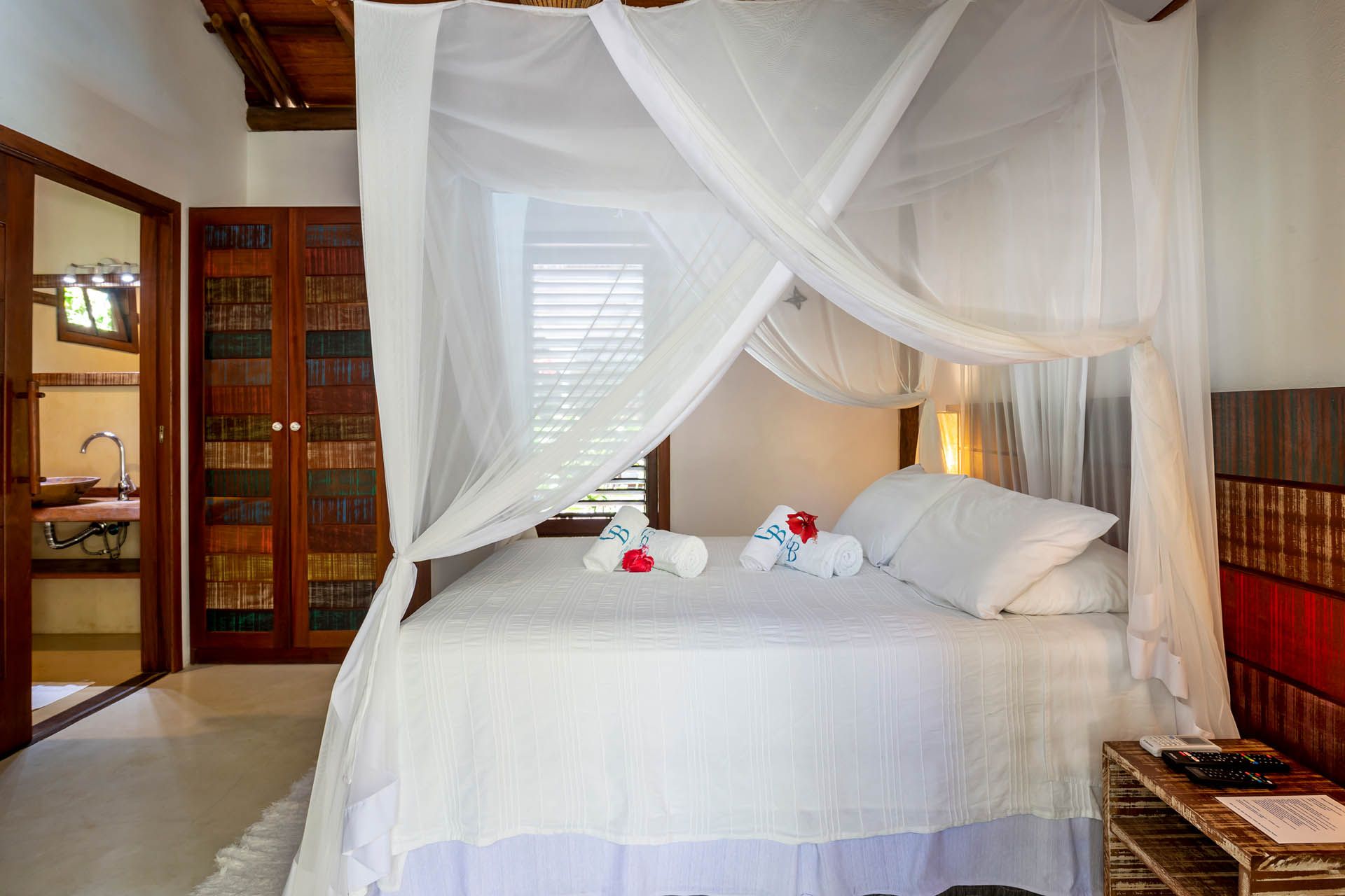 Cama de dossel branca em um quarto iluminado com cortinas transparentes, almofadas e cisnes de toalha sobre a cama.