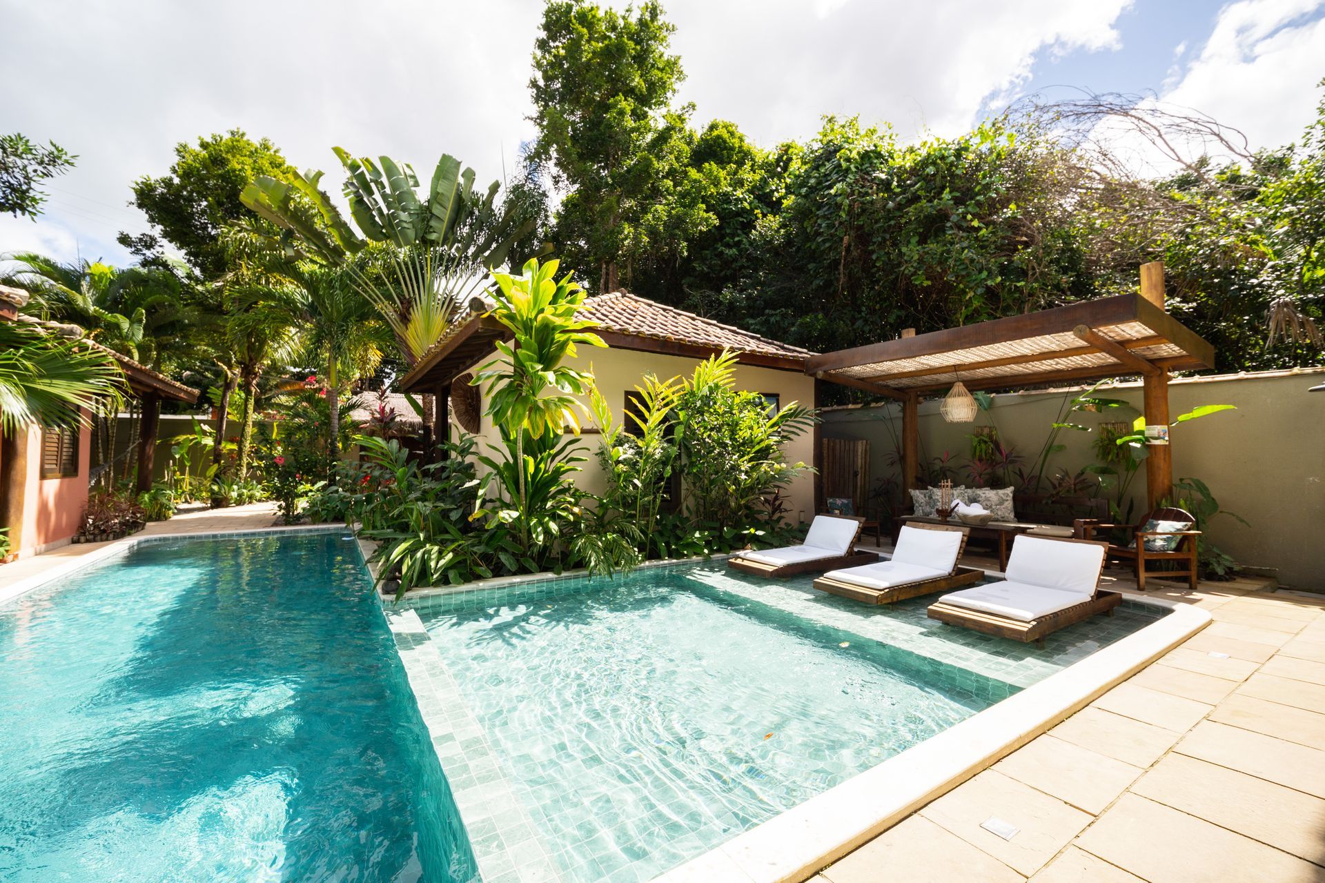 Pátio de uma villa de luxo com uma piscina azul brilhante ao entardecer, emoldurada por varandas com iluminação aconchegante e plantas tropicais.