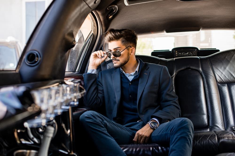 A Man in A Suit Is Sitting in The Back Seat of A Limousine — New Park Suit Hire & Menswear in Airlie Beach, QLD