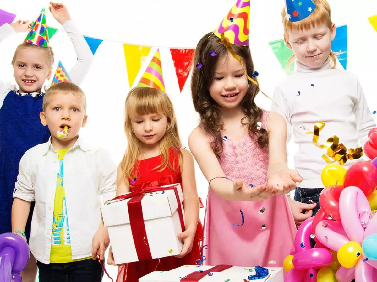 A group of children are celebrating a birthday with balloons and a cake.