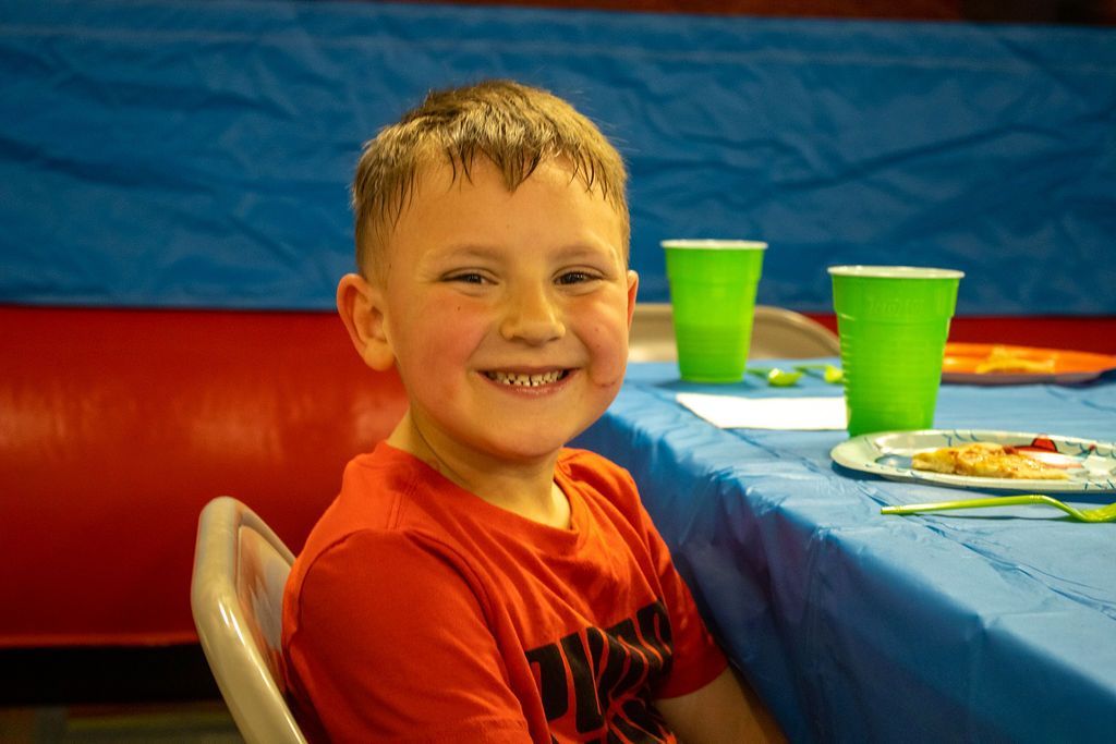 A young boy is sitting at a table with plates and cups at Impact Fun Zone