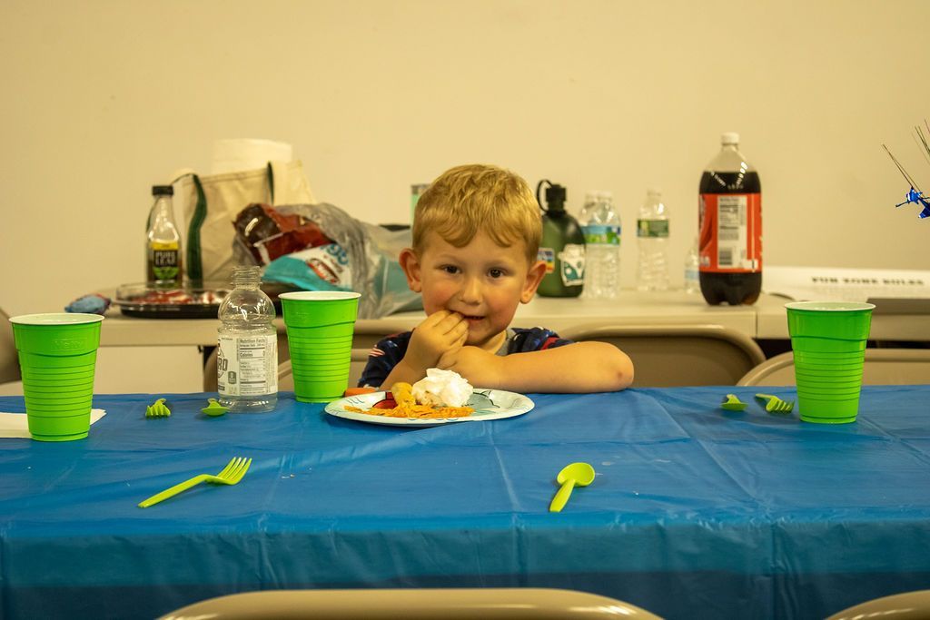 A young boy is sitting at a table with a plate of food at Impact Fun Zone