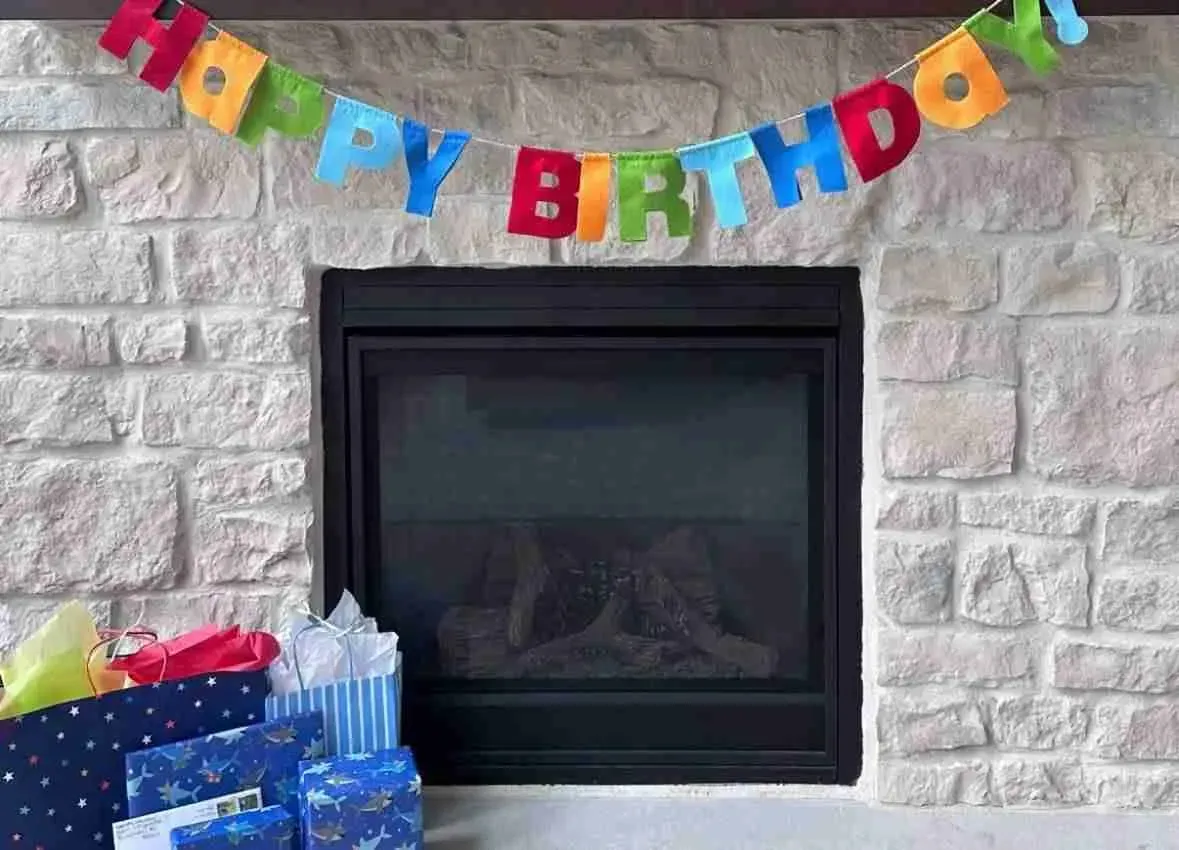 A happy birthday banner is hanging over a fireplace. A happy birthday banner is hanging over a fireplace.