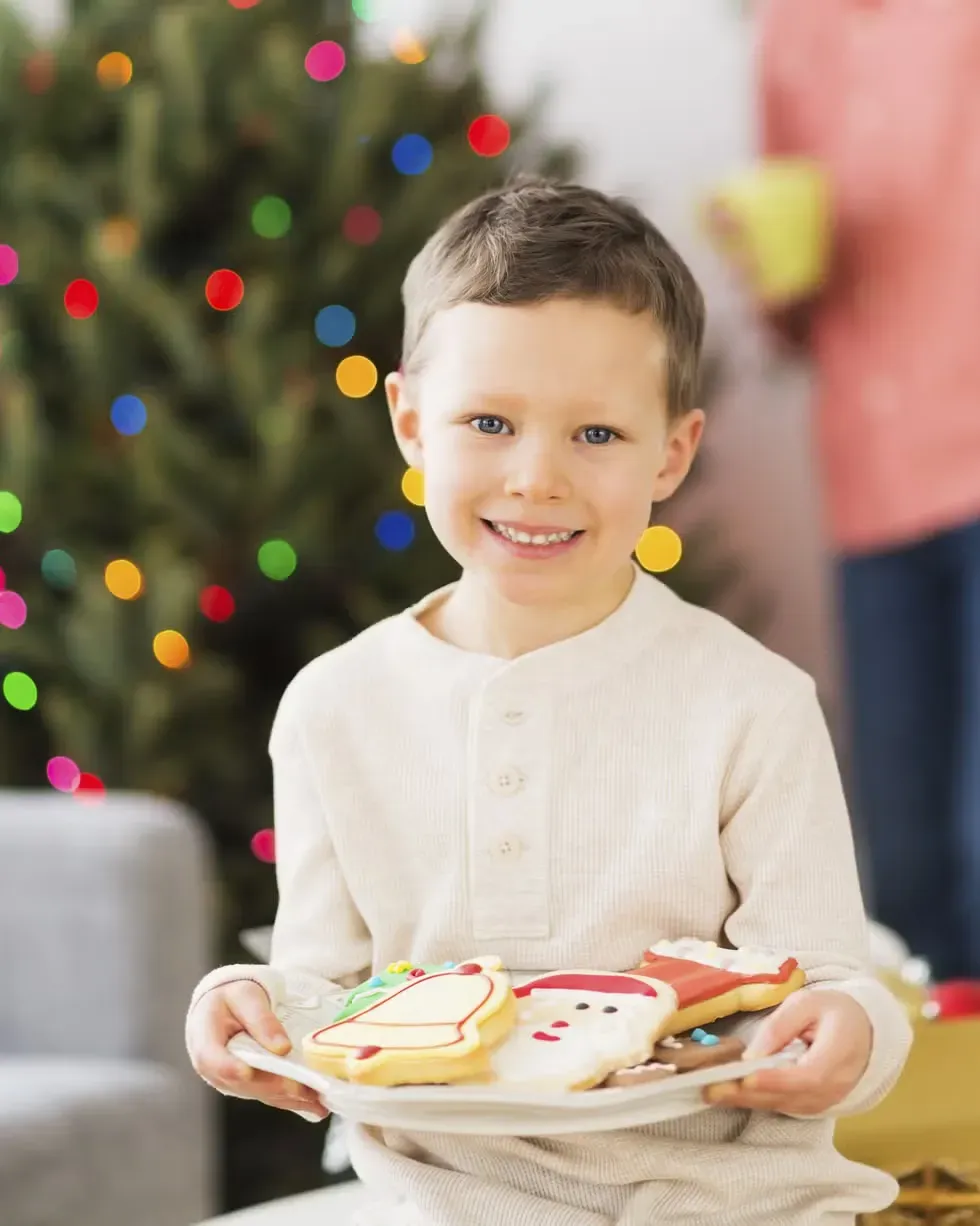 A young boy is holding a plate of christmas cookies.