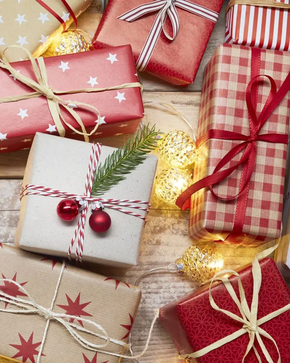 A pile of christmas presents wrapped in red and white paper on a wooden table.