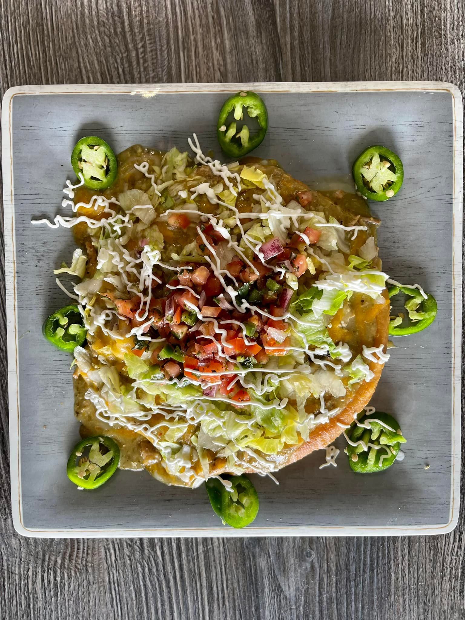 Sliced jalapeños around a colorful taco on a square gray plate with sauce drizzle