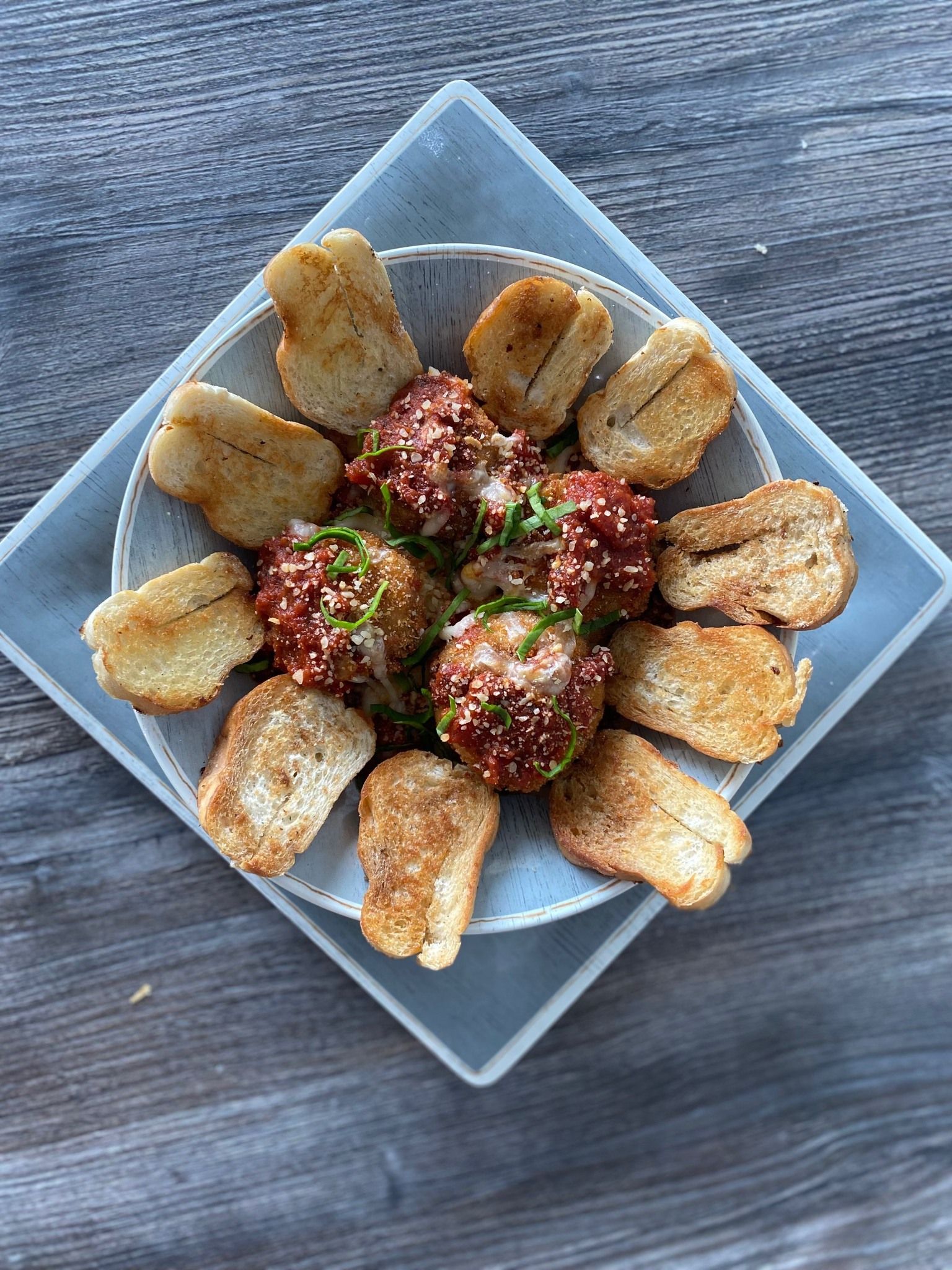 Plated appetizer with fried wedges around three herb-topped meatballs on a square white dish.