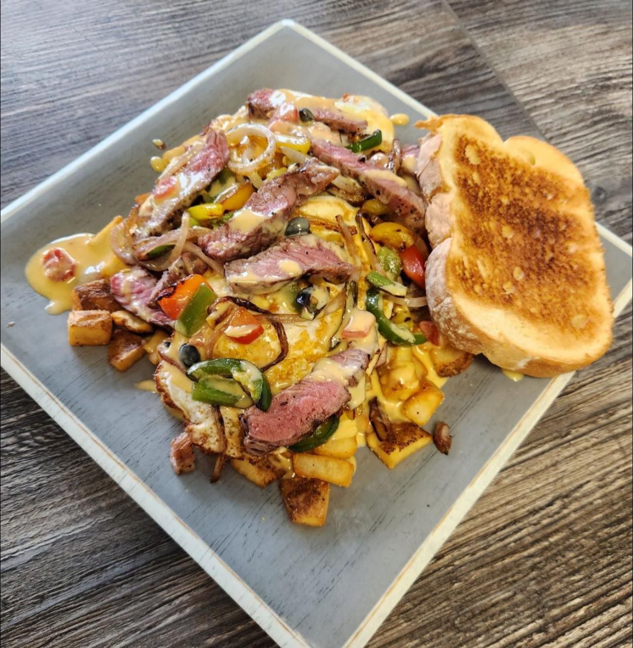 Loaded nachos topped with melted cheese, peppers, and meat, with a toasted bread slice on a square plate.
