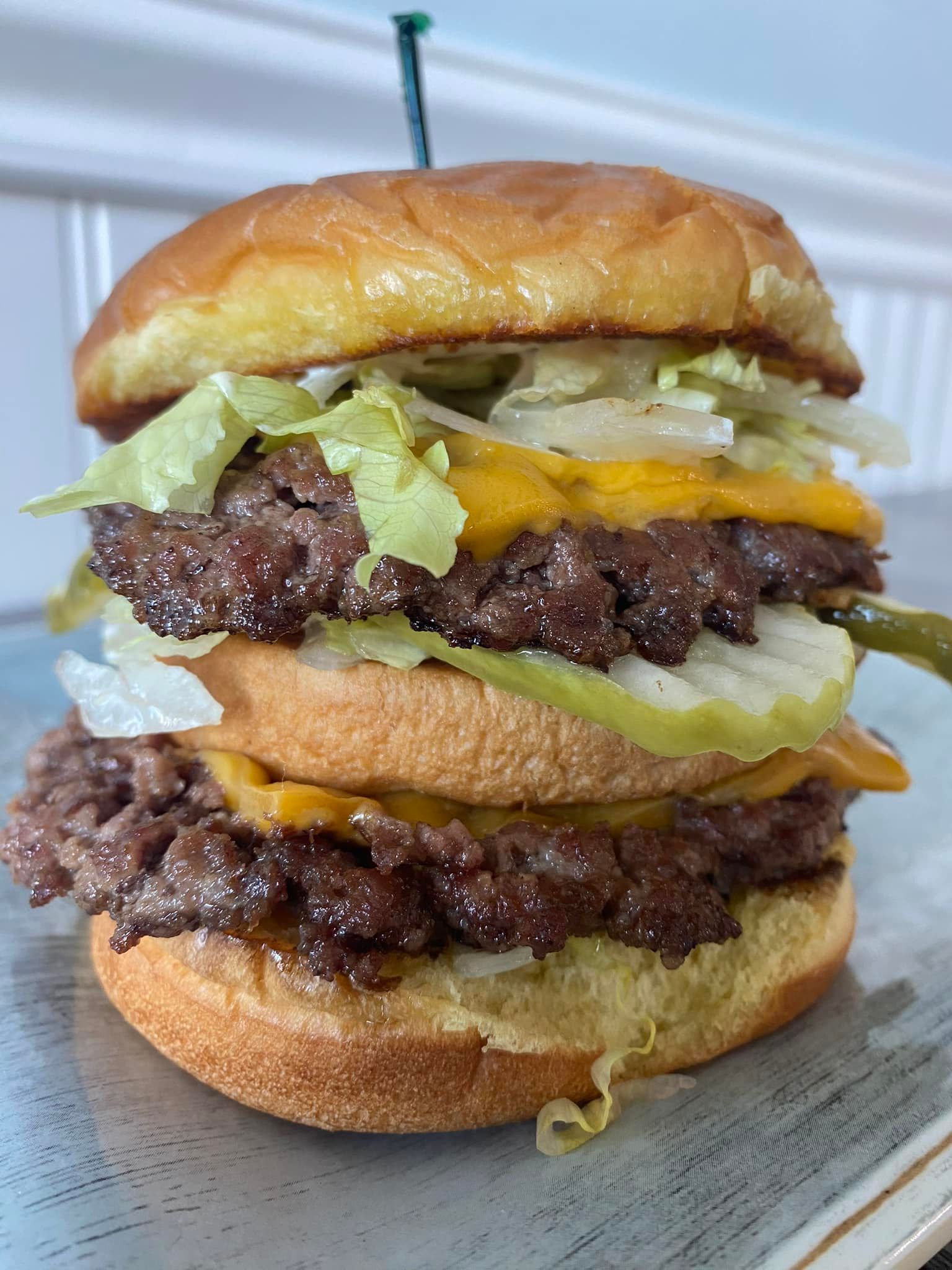 Close-up of a stacked cheeseburger with lettuce and melted cheddar on a paper tray.