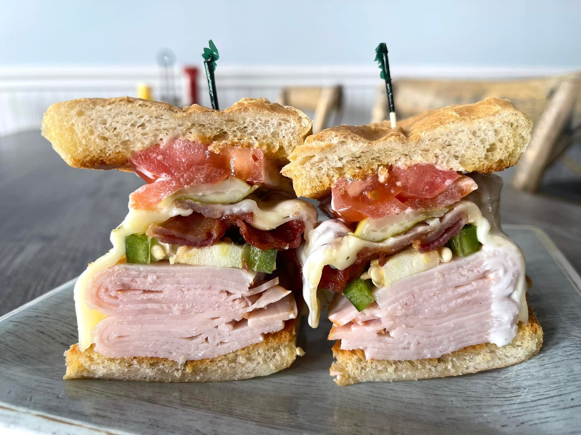 Close-up of a stacked deli sandwich cut in half, showing ham, vegetables, and toasted bread on a wooden board