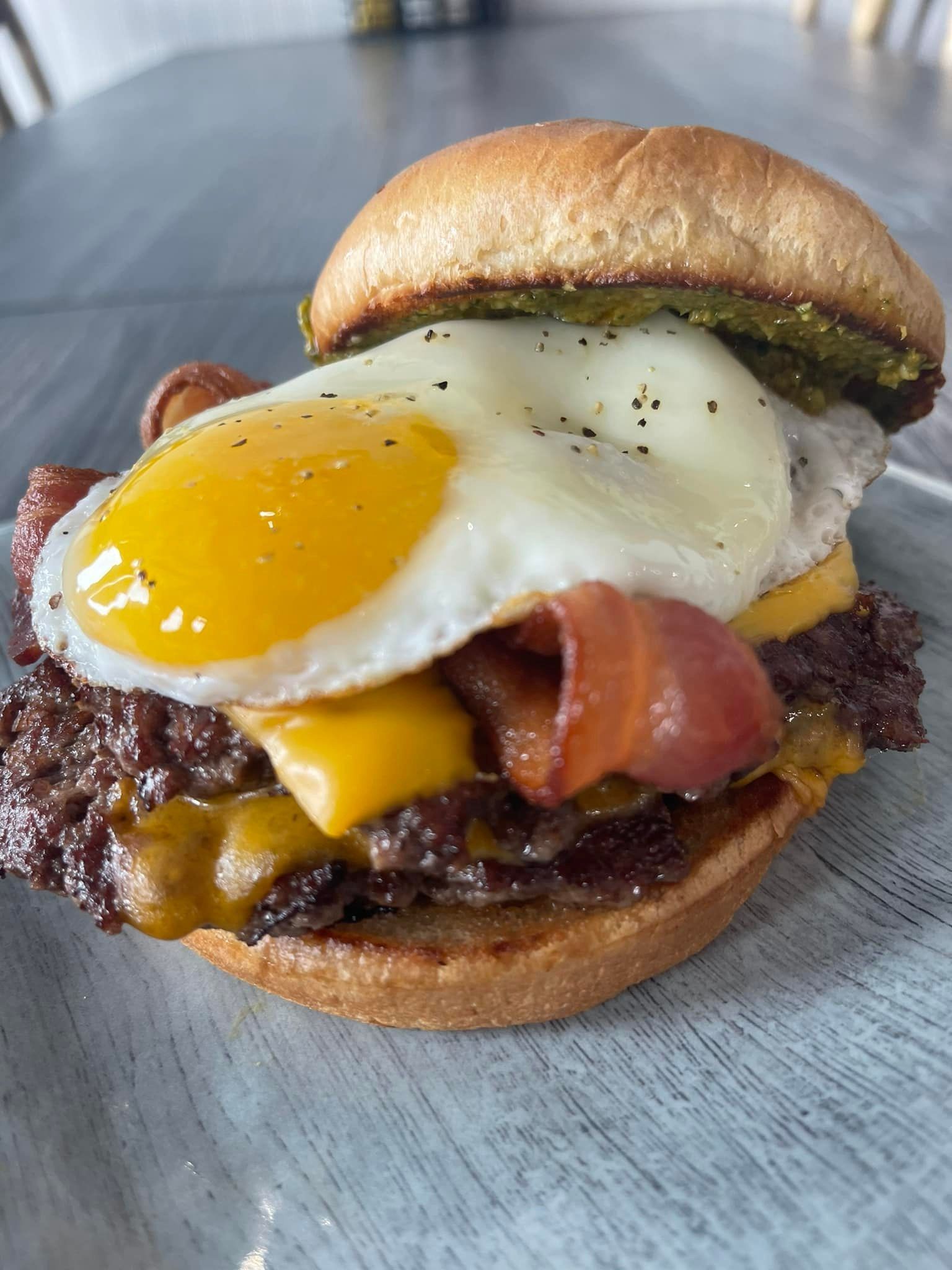 Bacon cheeseburger with a fried egg on a bun, served on a gray plate.