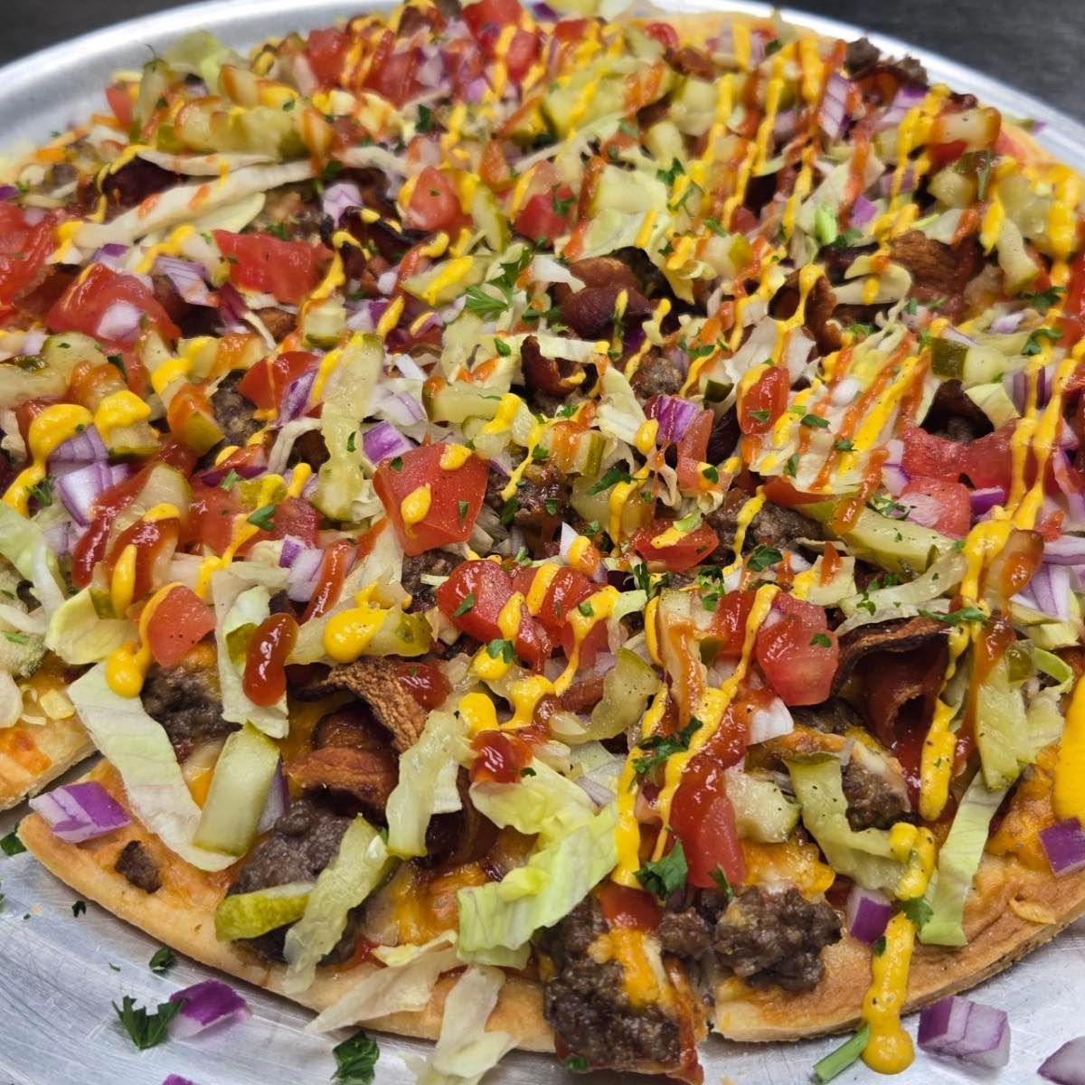 Loaded nachos with lettuce, tomatoes, yellow sauce, cheese, and seasoned meat on a round tray.