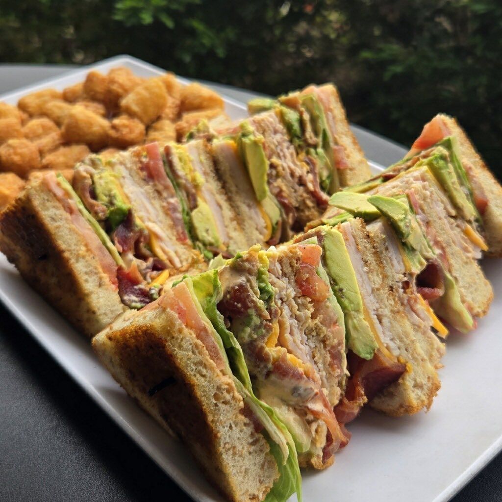 Club sandwich wedges with fries on a white plate outdoors