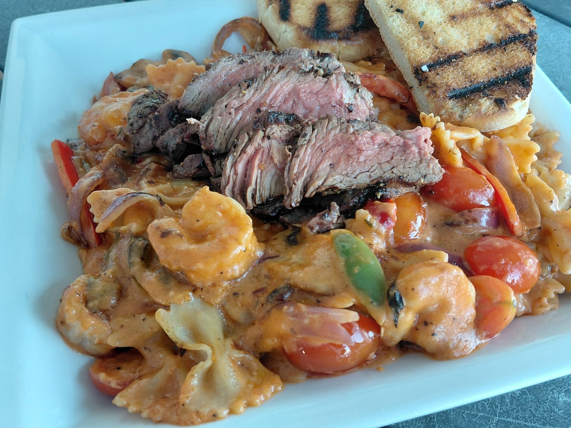 Grilled steak over creamy pasta with cherry tomatoes and toasted bread on a white plate