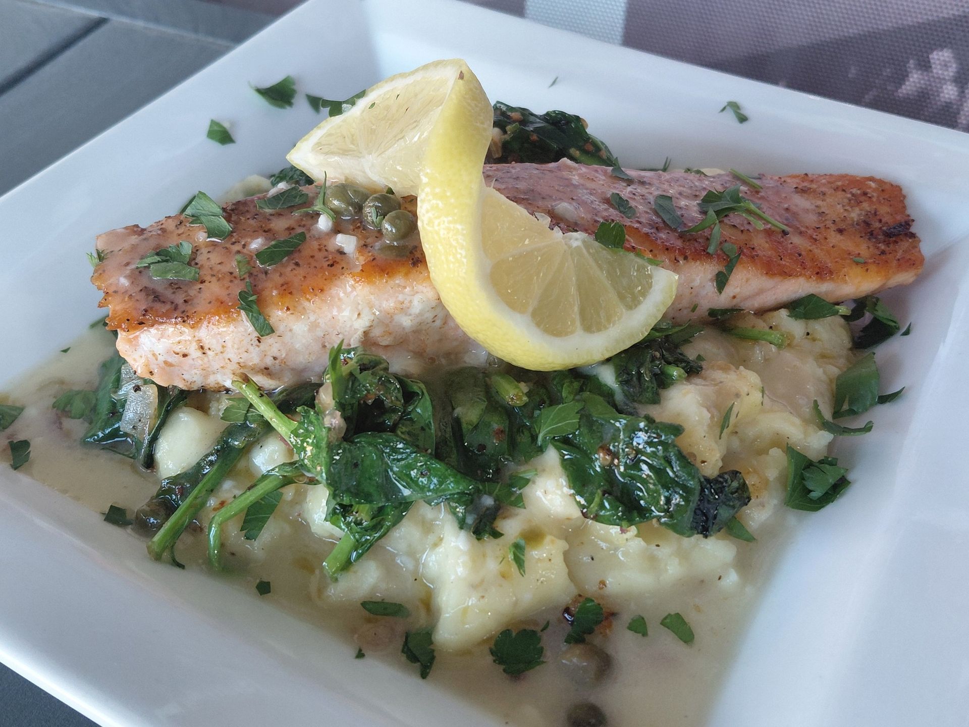 Grilled salmon fillet on creamy risotto with greens, garnished with lemon wedges on a white plate