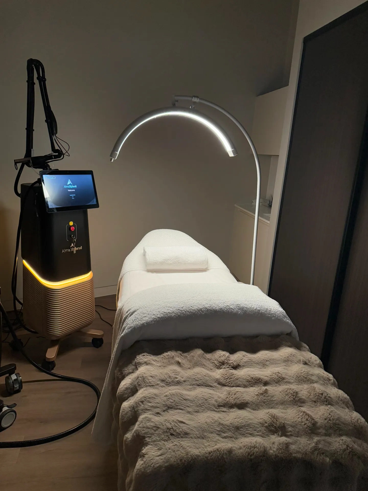 Treatment room with a bed, medical device, and curved lighting.
