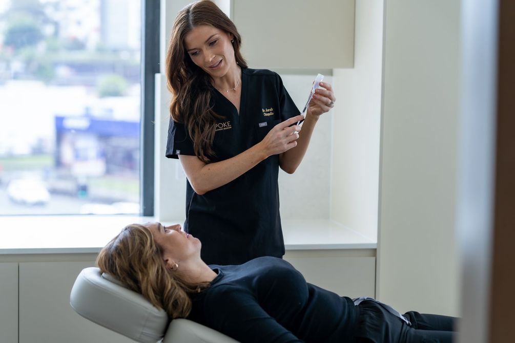 Woman in black uniform preparing injection for patient in a medical setting.