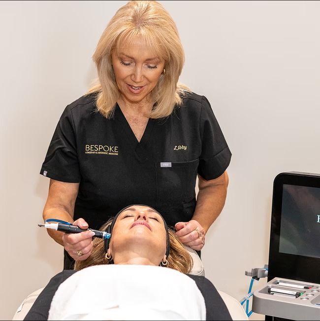 Woman administering facial treatment to another woman in a medical setting.
