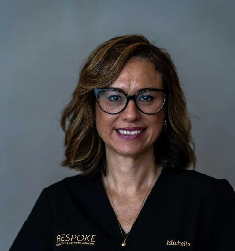 Woman with glasses smiles, wearing black scrubs with 